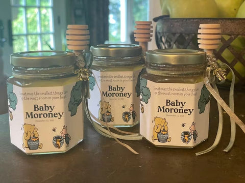 Three jars of honey with wooden dipper sticks and Winnie the Pooh labels on a wooden surface.
