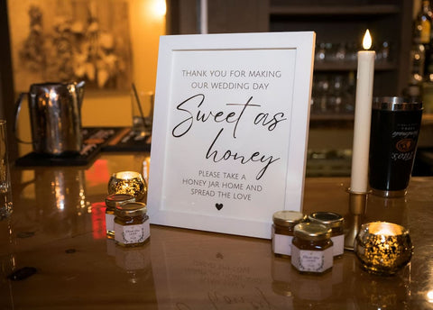 Wedding reception table with honey jars and a sign thanking guests for spreading love.