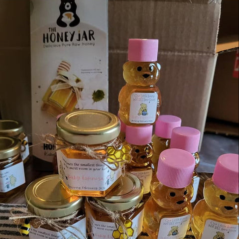 Honey jars and bear-shaped bottles with caps on a striped surface, with 'The Honey Jar' brand visible.