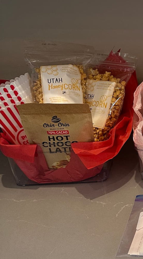 Snack basket with Utah honey corn, hot chocolate mix, and other treats on a gray surface.