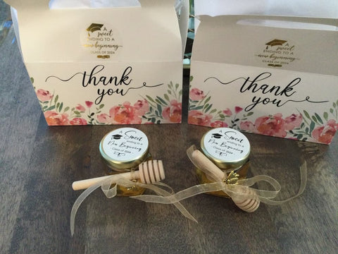 Two small jars of honey with wooden dipper sticks in front of 'thank you' boxes with floral designs.
