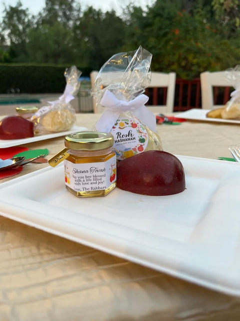Small jar of honey and a piece of fruit on a white plate with a blurred outdoor background