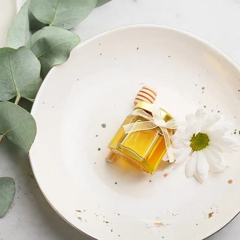 Honey jar with a white flower and green leaves on a white plate