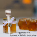 Jar of honey with a honey dipper, bee charm, and white ribbon on blurred background