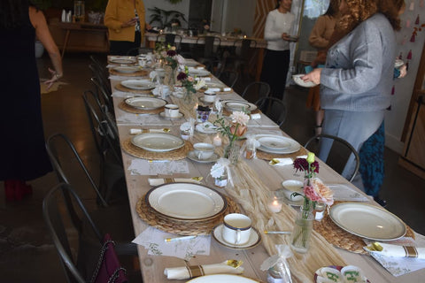 Dining table set for a meal with plates, cups, small honey jars, and floral arrangements in a casual indoor setting