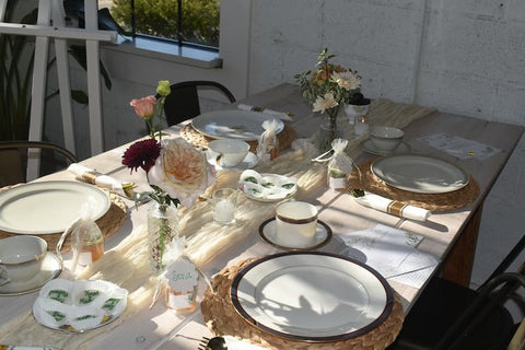 Dining table set with plates, glasses, flowers, and small honey jars in an outdoor setting.