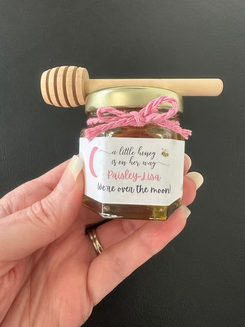 Hand holding a small jar of honey with a pink label against a dark background