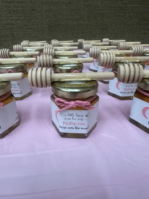 Jars of honey with wooden dipper sticks on a pink surface