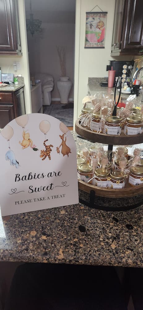 Baby shower treat table with honey jars and a sign on a kitchen counter.