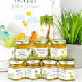 Jars of baby shower honey with personalized labels on a white surface.