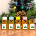 Five bear-shaped honey jars with colorful lids on a wooden surface with a Christmas tree in the background.