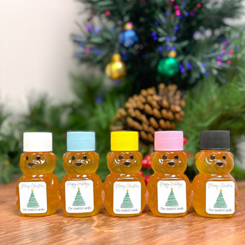 Five bear-shaped honey jars with colorful lids on a wooden surface, Christmas tree in the background
