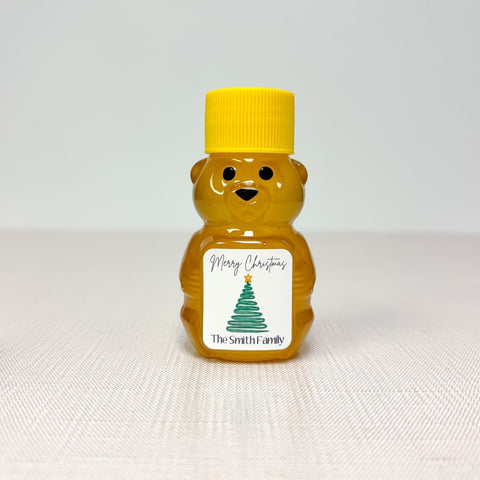 Bear-shaped honey container with Christmas tree label and yellow cap on white background
