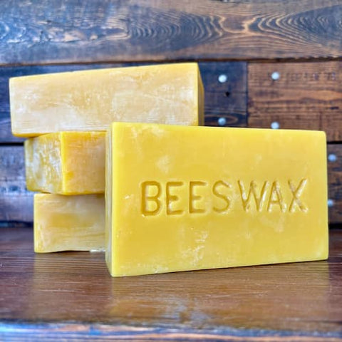 Three 1 pound bars of beeswax on a wooden surface