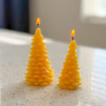 Two yellow tree-shaped candles on a light surface with a blurred background