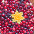 Cranberries floating in water with a yellow snowflake-shaped candle in the middle, all on a wooden surface.