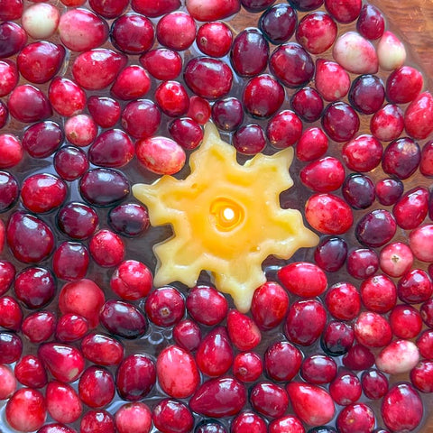 Cranberries floating in water with a yellow snowflake-shaped candle in the middle, all on a wooden surface.