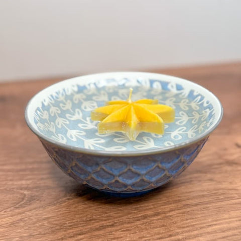 Yellow flower-shaped candle floating in water in a decorative ceramic bowl on a wooden surface