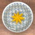 Yellow star-shaped candle floating in water in a decorative bowl with a leaf pattern