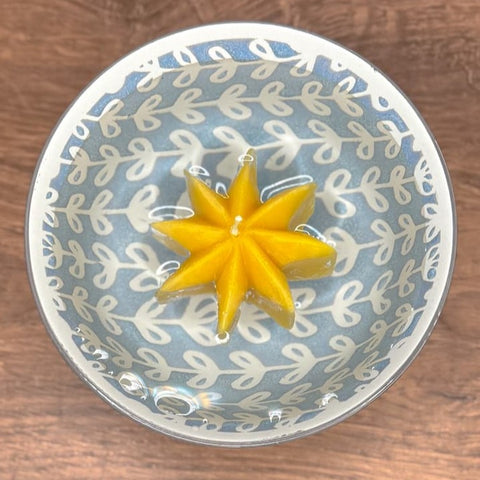 Yellow star-shaped candle floating in water in a decorative bowl with a leaf pattern