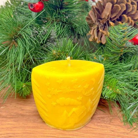Yellow textured candle on a wooden surface with Christmas decorations in the background