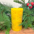 Yellow candle with a snowflake pattern on a wooden surface with greenery and berries