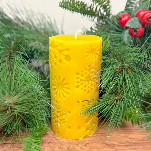 Yellow candle with a snowflake pattern on a wooden surface with greenery and berries