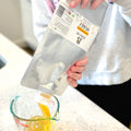 Person pouring honey from a Mylar bag into a measuring cup on a kitchen counter.