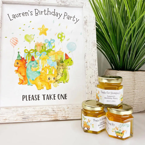 Decorative sign for a birthday party with dinosaur illustrations, accompanied by honey jars with personalized labels.