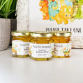 Three jars of honey with personalized labels on a white surface, with dinosaur-themed decorations in the background.