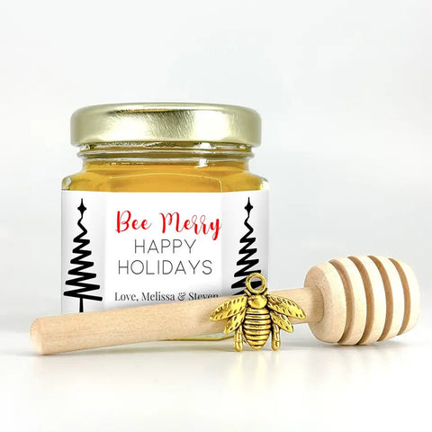 Jar of honey with a gold lid, gold bee charm, and wooden honey dipper on a white background