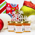 Three jars of honey with 'Bee Merry' labels, surrounded by Christmas decorations.