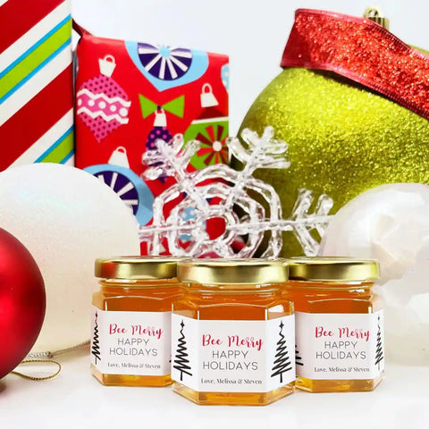 Three jars of honey with 'Bee Merry' labels, surrounded by Christmas decorations.