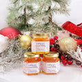 Jars of honey with decorative labels in front of a Christmas tree and ornaments.