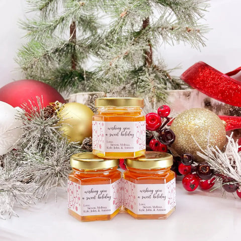 Jars of honey with decorative labels in front of a Christmas tree and ornaments.