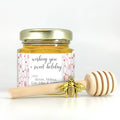 Jar of honey with a decorative label and wooden honey dipper on a white background