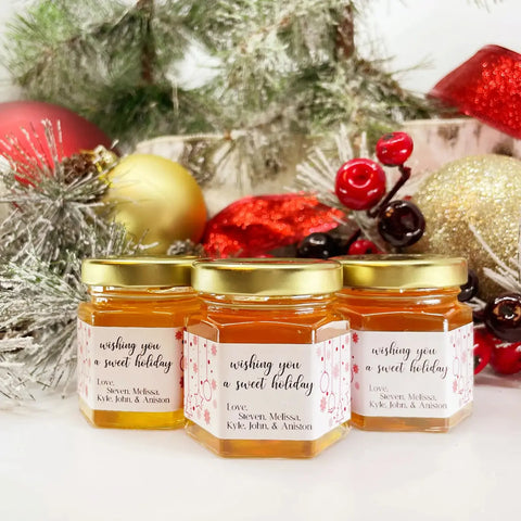 Three jars of honey with personalized labels in front of Christmas decorations.