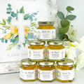 Jars of honey with personalized labels on a decorative background with flowers and a cross.