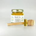 Jar of honey with a personalized label and wooden honey dipper and thank you charm on a light gray background
