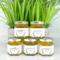 Five jars of honey stacked with a plant in the background