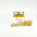 Jar of honey with a floral label and wooden honey dipper on a white background