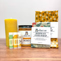Yellow beeswax candle, jar of honey, beeswax lip balms, and various beeswax food wraps on a wooden surface.