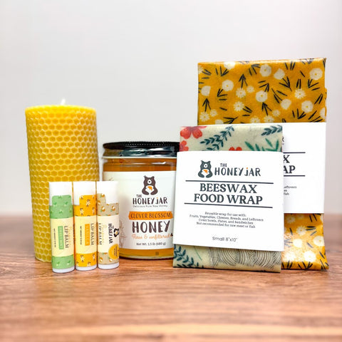 Yellow beeswax candle, jar of honey, beeswax lip balms, and various beeswax food wraps on a wooden surface.