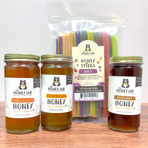 Three jars of honey and a package of honey sticks on a wooden surface.