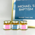 Three small jars with personalized labels in front of a baptism sign.