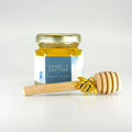 Jar of honey with a personalized label and wooden honey dipper on a light background