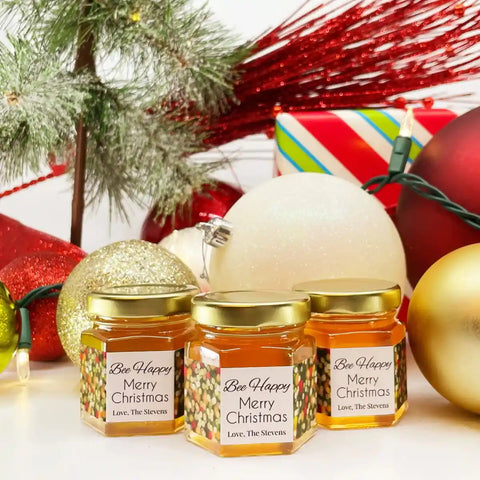 Three jars of 'Bee Happy' honey with decorative labels on a festive background with ornaments and lights.