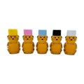 Five bear-shaped honey-filled bottles with colored caps on a white background