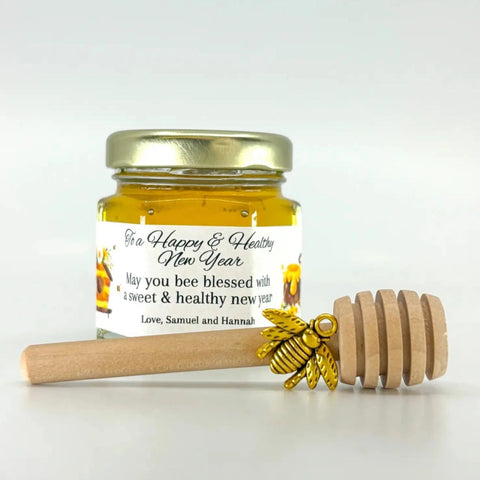 Jar of honey with a decorative label and wooden honey dipper on a white background