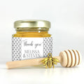 Jar of honey with a gold lid and wooden dipper on a white background